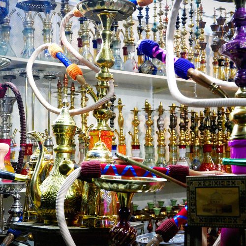 Display of ornate brass hookahs with colorful hoses and decorative elements in Middle Eastern shop, Berlin