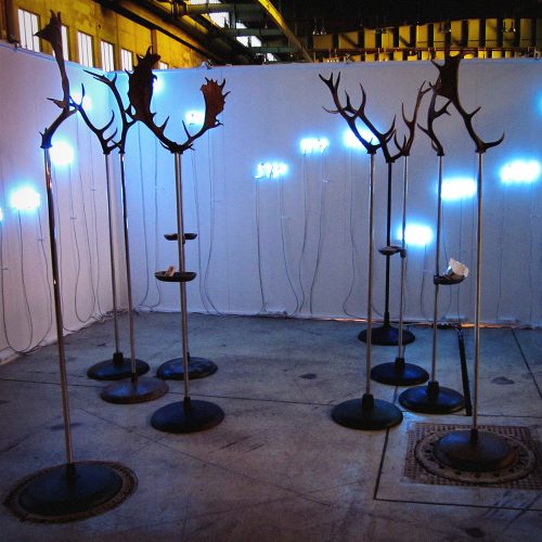 Contemporary art installation with glowing blue lights and metal tree branch sculptures in industrial warehouse space, Berlin