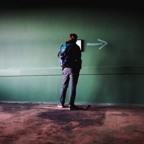 Person viewing minimalist wall installation with arrow pointing right in studio space, Berlin