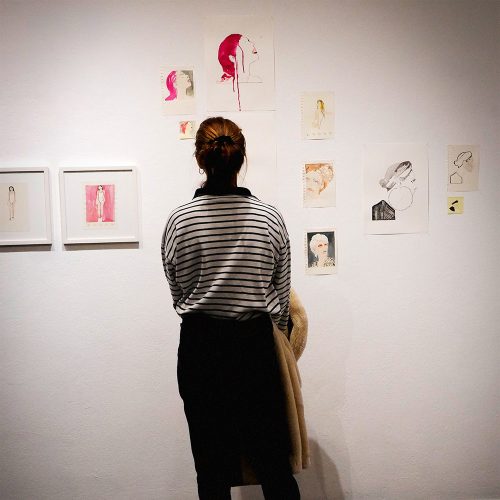 Person viewing gallery wall with framed portrait sketches and figurative drawings, Berlin art exhibition